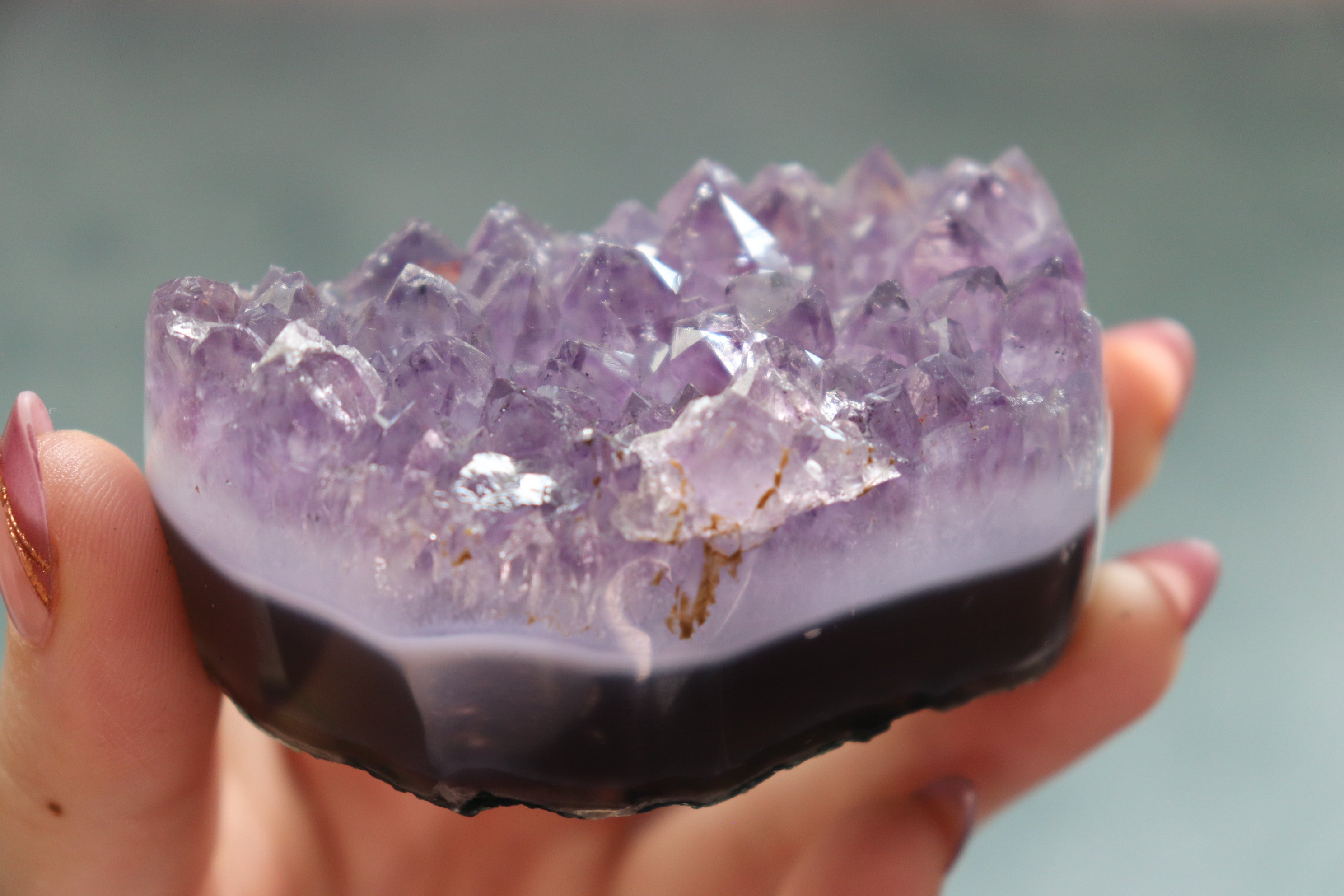 Amethyst crystal bowl held in a hand against a blurred background