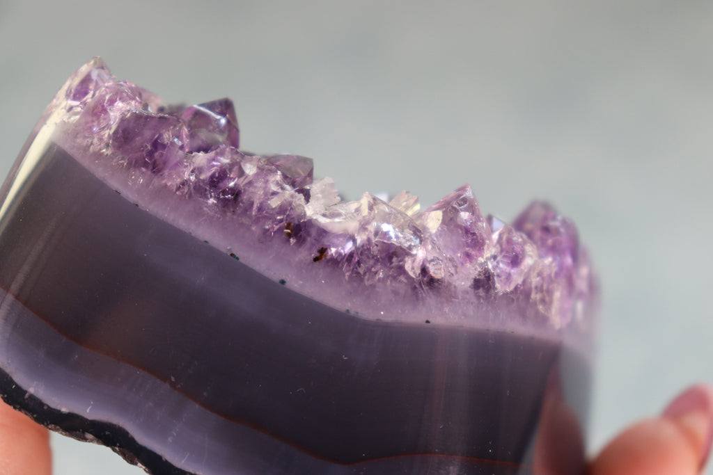 Amethyst On a Agate base crystal  held by a hand against a neutral background