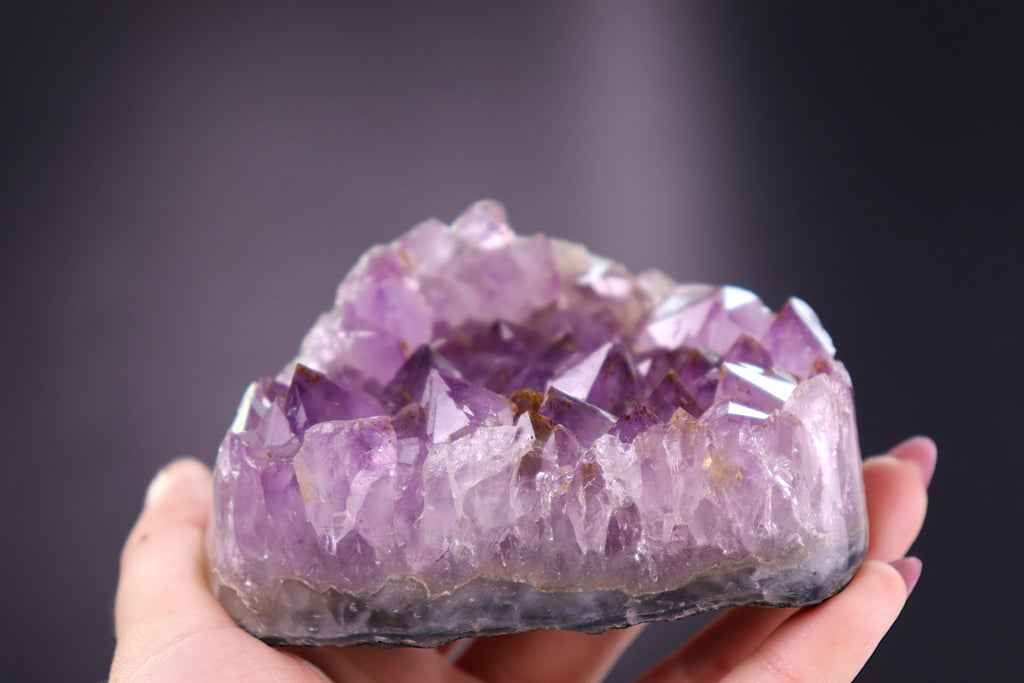 Amethyst crystal held in a hand against a dark background