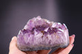 Amethyst crystal held in a hand against a dark background