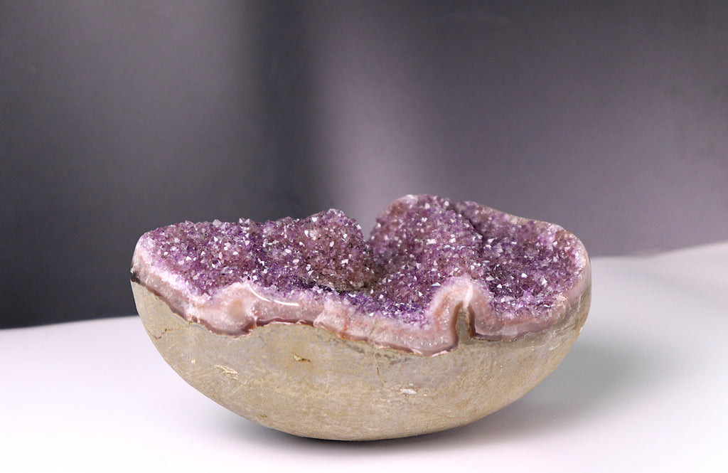 Amethyst geode on a white surface with a dark background