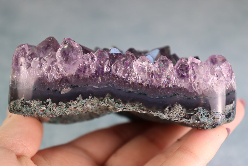 Amethyst crystal on moss agate held in a hand against a neutral background
