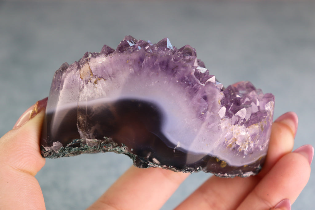 Amethyst crystal held in a hand against a neutral background