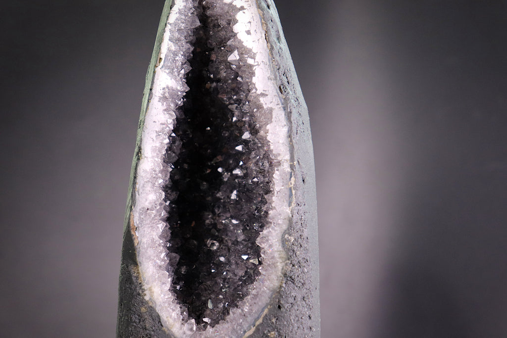 Close-up of a amethyst crystal with a dark core and white calcite mineral deposits on a gray background