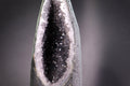 Close-up of a amethyst crystal with a dark core and white calcite mineral deposits on a gray background