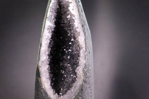 Close-up of a amethyst crystal with a dark core and white calcite mineral deposits on a gray background