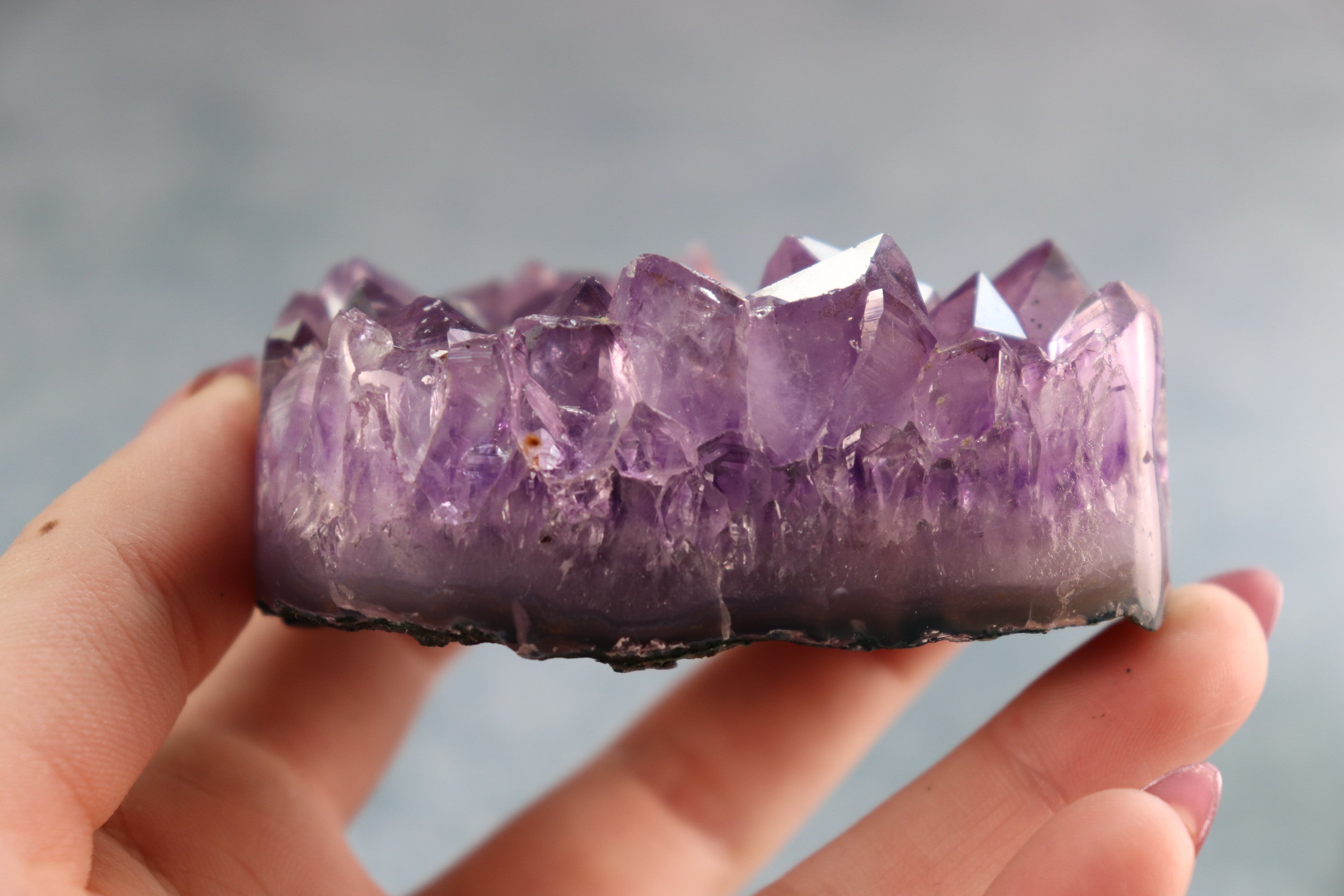 Amethyst crystal held in a hand against a blurred background