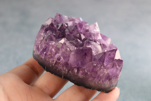 Amethyst crystal cluster held in a hand against a blurred background