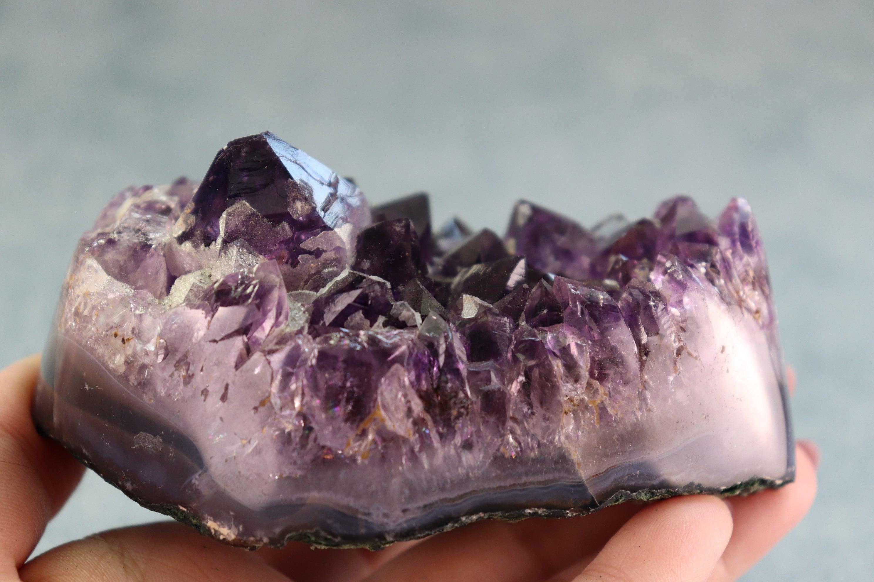 Amethyst crystal held in hand against a neutral background
