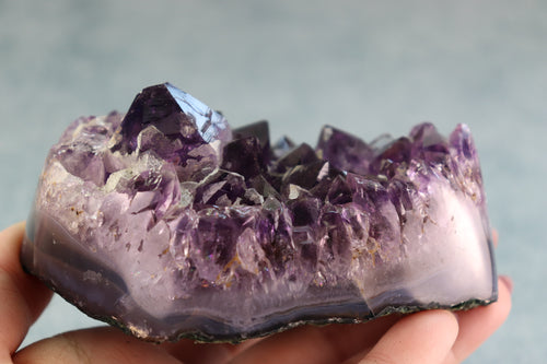 Amethyst crystal held in hand against a neutral background