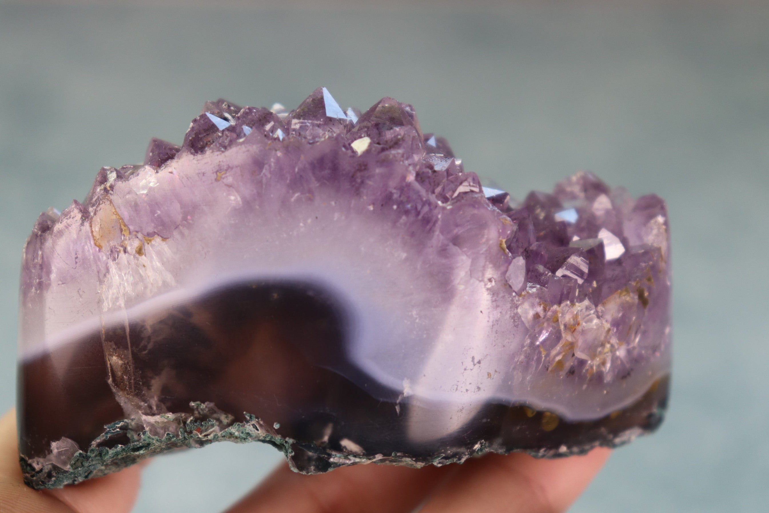 Amethyst crystal with agate base held in hand against a neutral background