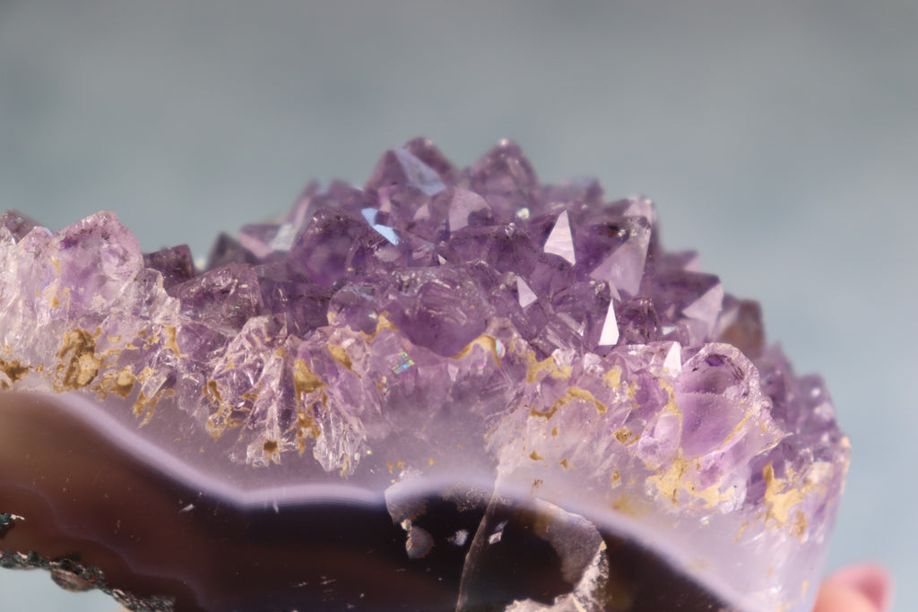 Close-up of a purple amethyst crystal formation with gold inclusions on a blurred background
