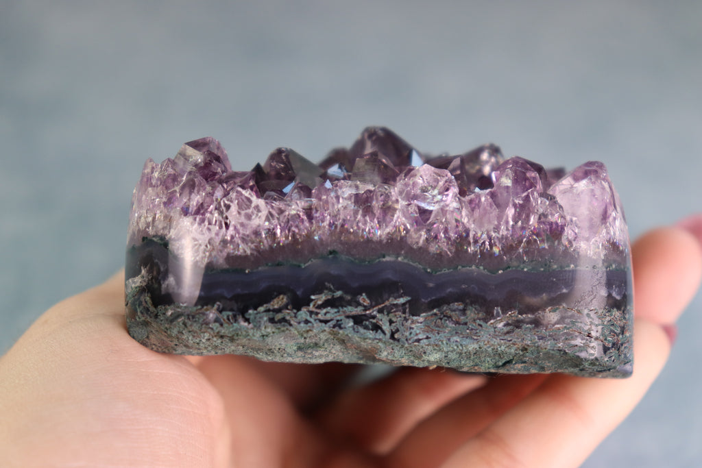 Amethyst on moss agate crystal formation held in a hand against a neutral background