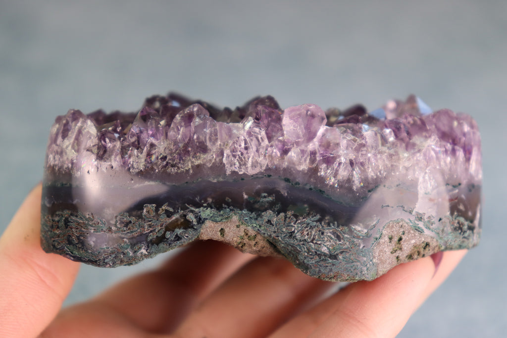 Amethyst crystal held in a hand against a neutral background