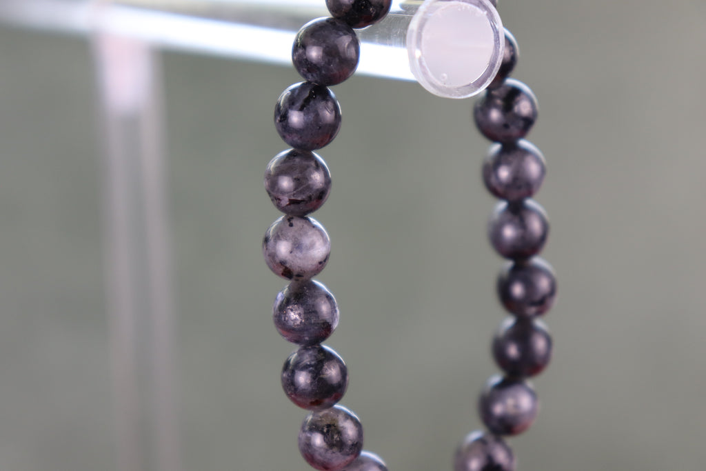 Larvikite Black Beads with flash of silver and color on a stand with a blurred background