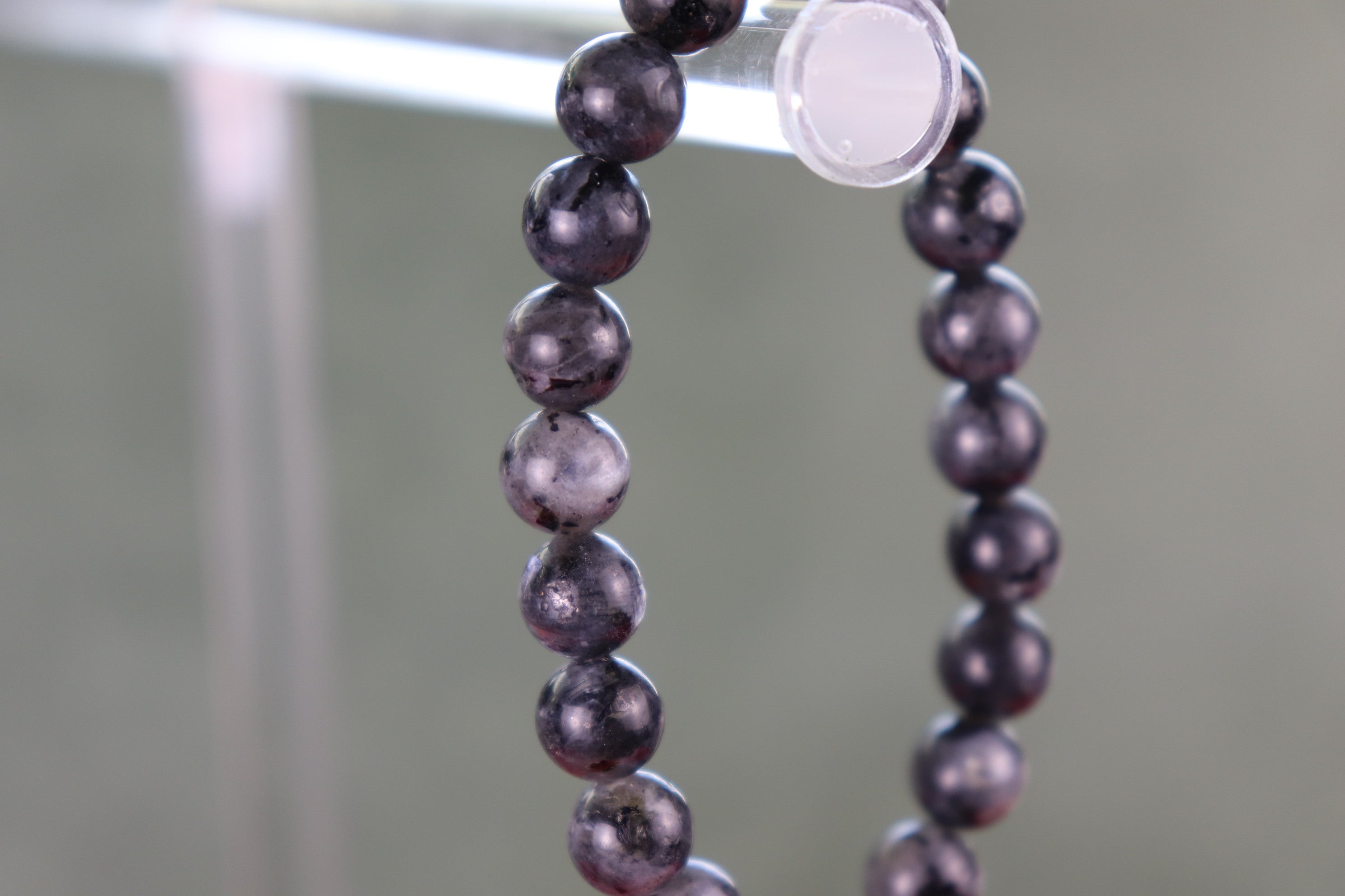Larvikite Black Beads with flash of silver and color on a stand with a blurred background