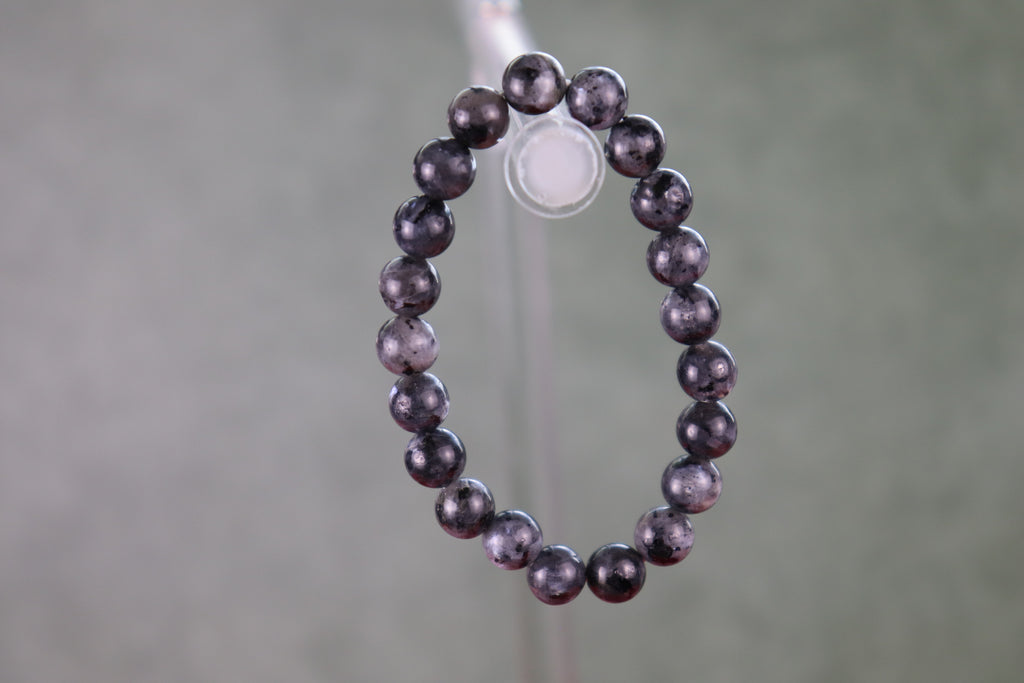 Larvikite Black Beads with flash of silver and color on a stand with a blurred background