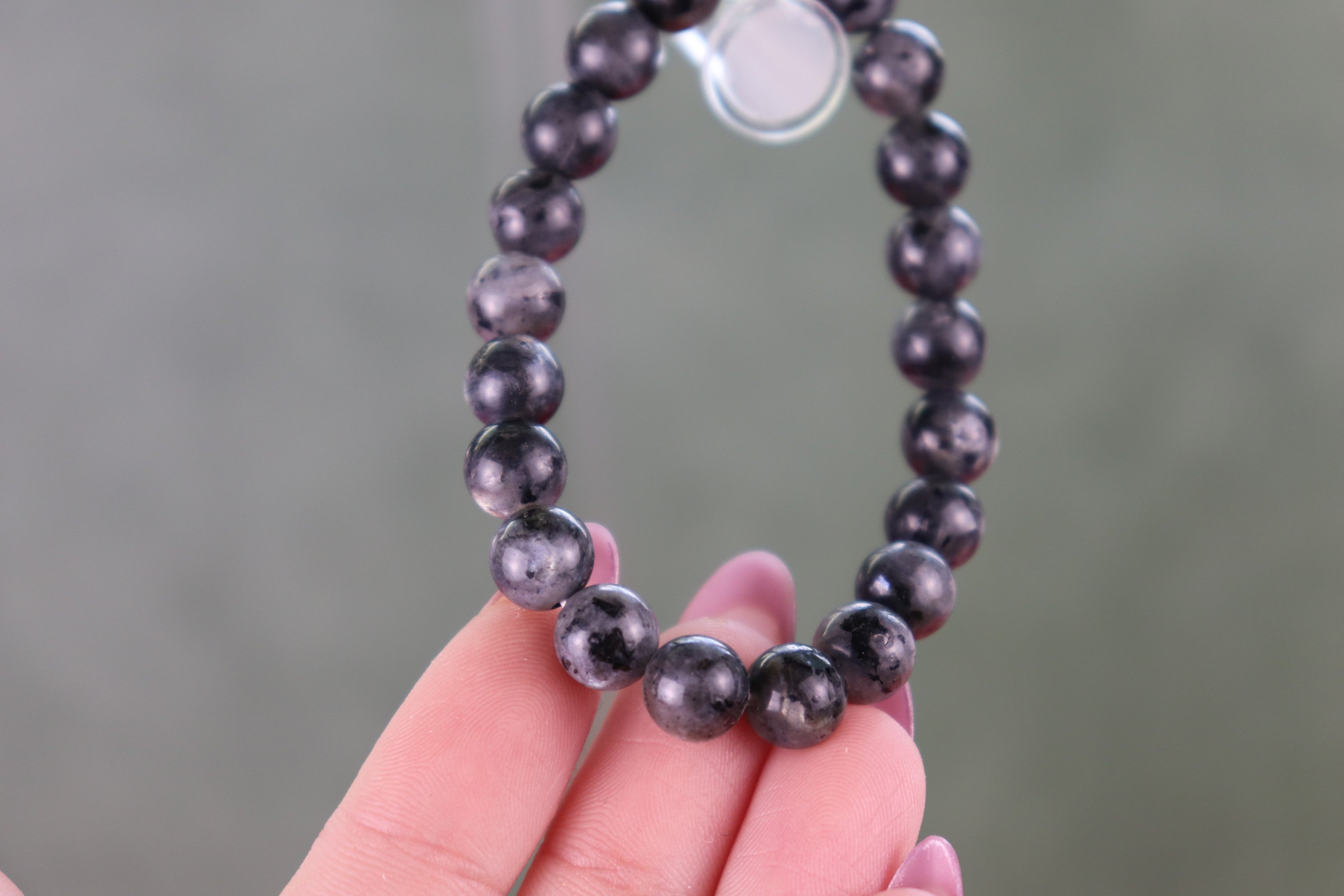 Black beaded Larvikite bracelet held by a hand against a blurred background