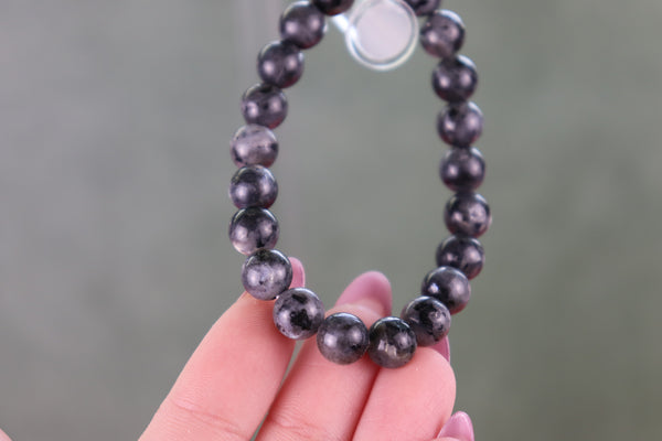 Black beaded Larvikite bracelet held by a hand against a blurred background