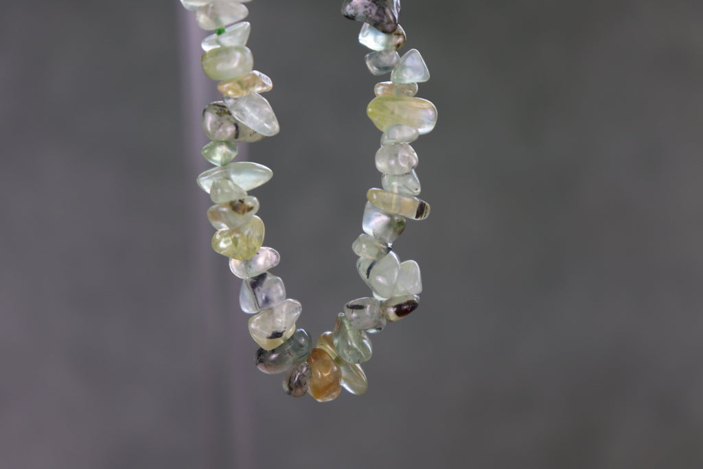 Bracelet with small, multicolored Prehnite gemstones against a gray background