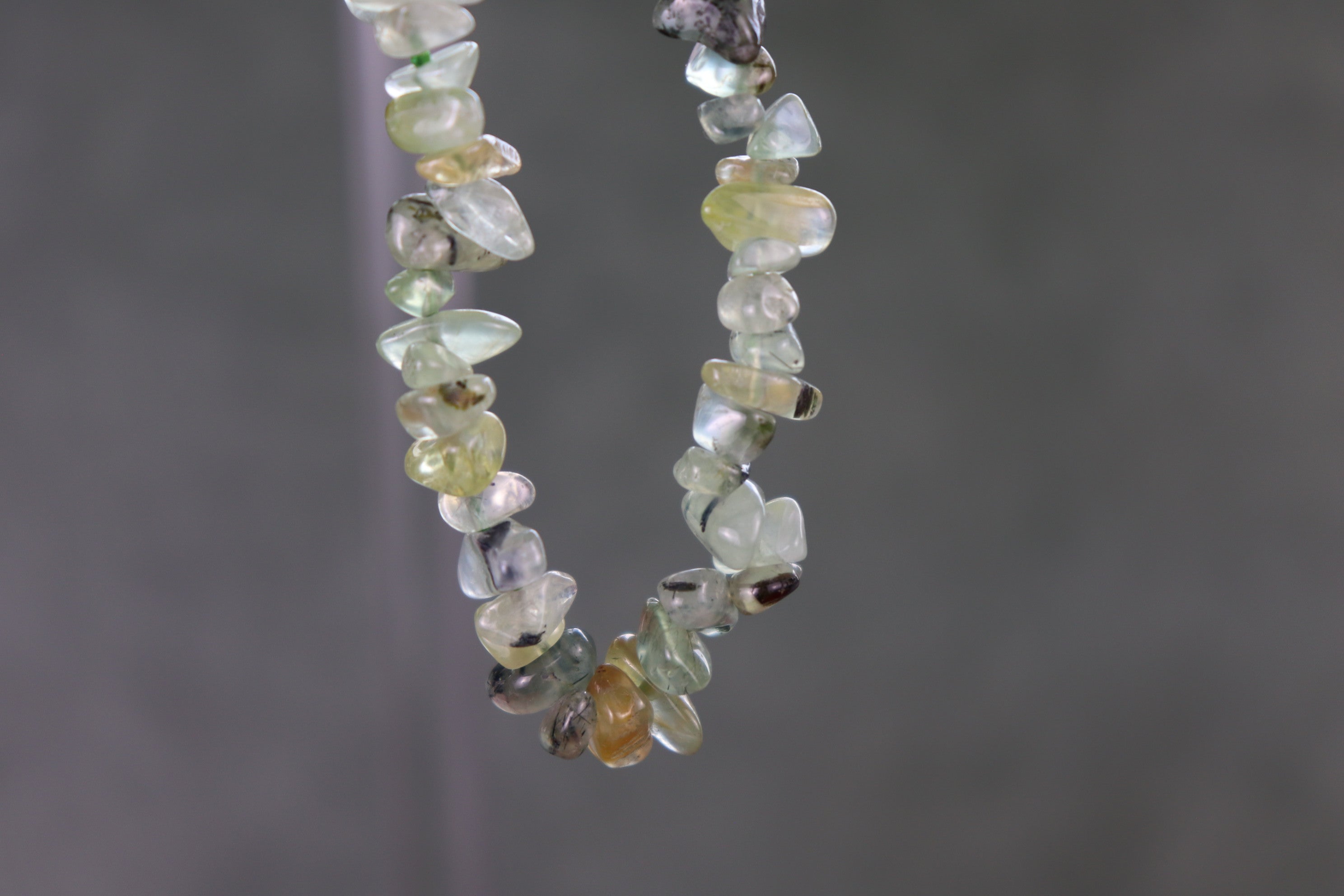 Bracelet with small, multicolored Prehnite gemstones against a gray background