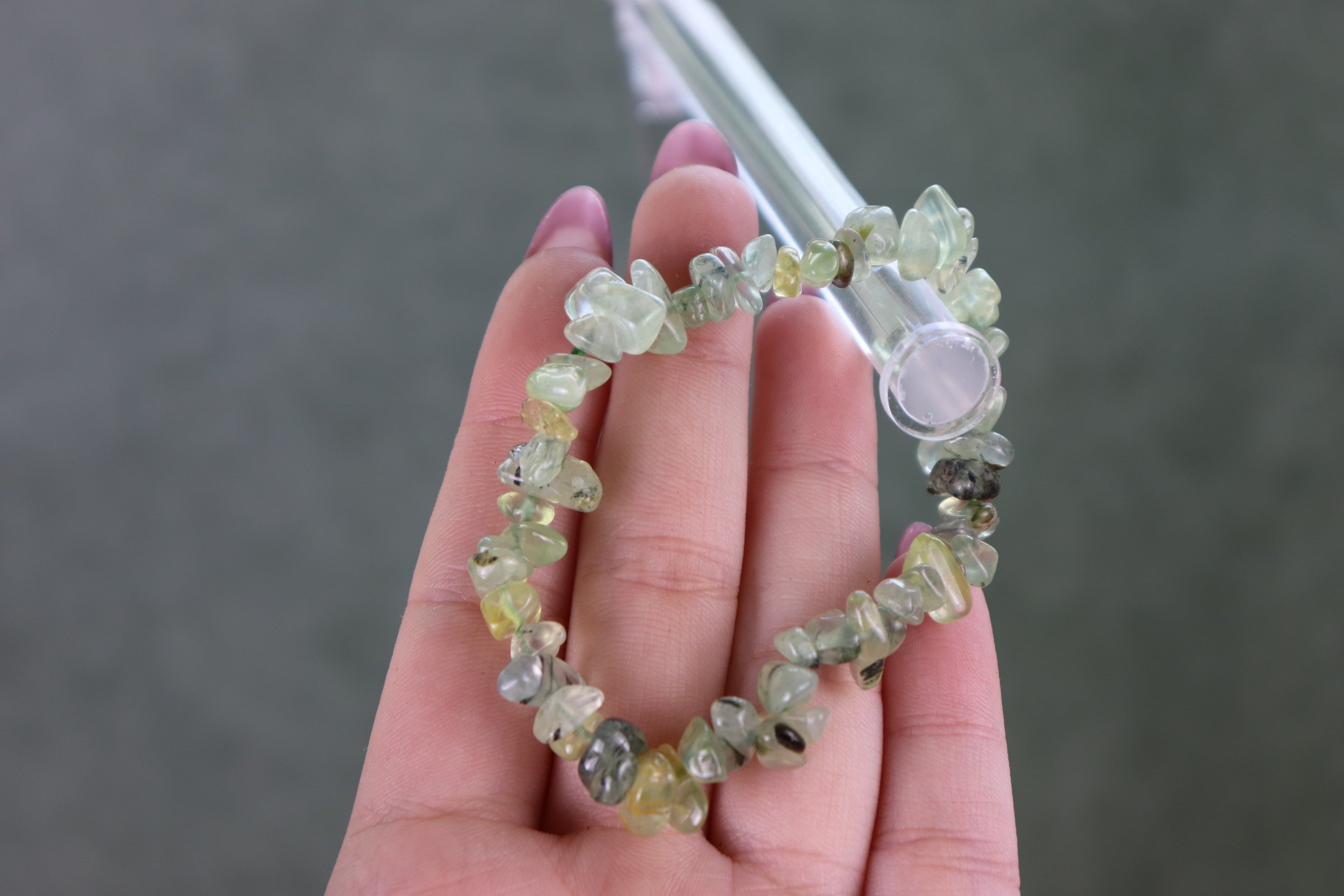 Prehnite beaded bracelet held in a hand against a neutral background