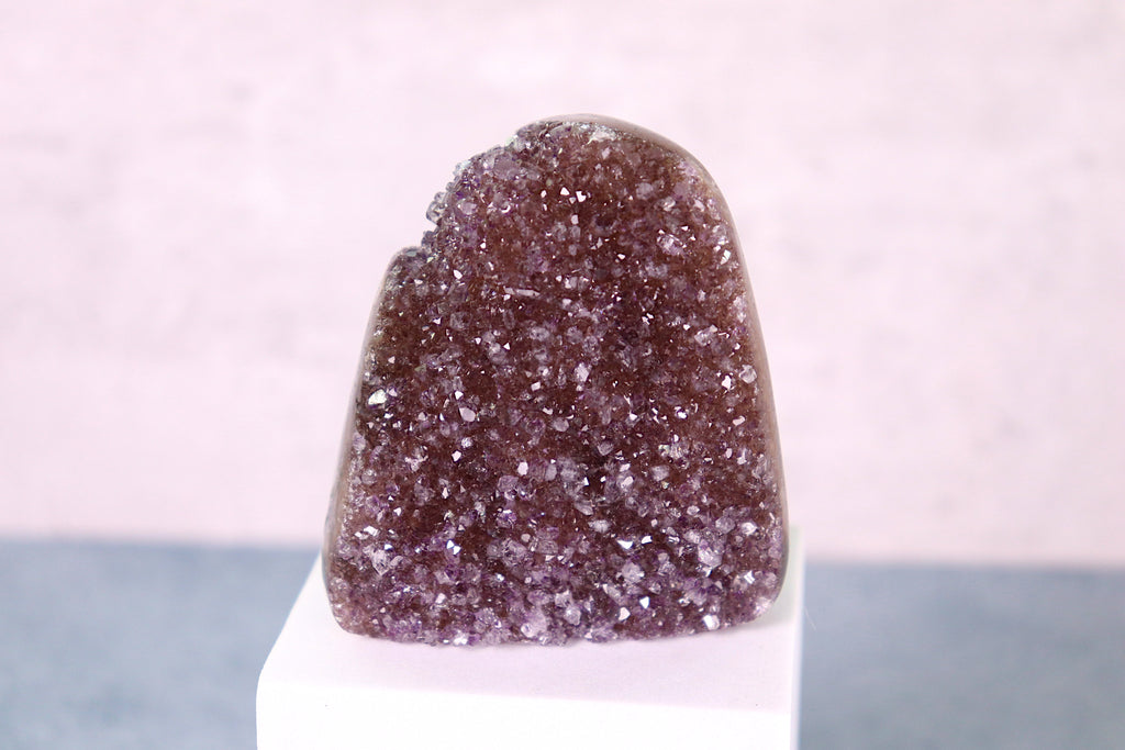 Amethyst  crystal on a white stand with a light pink background