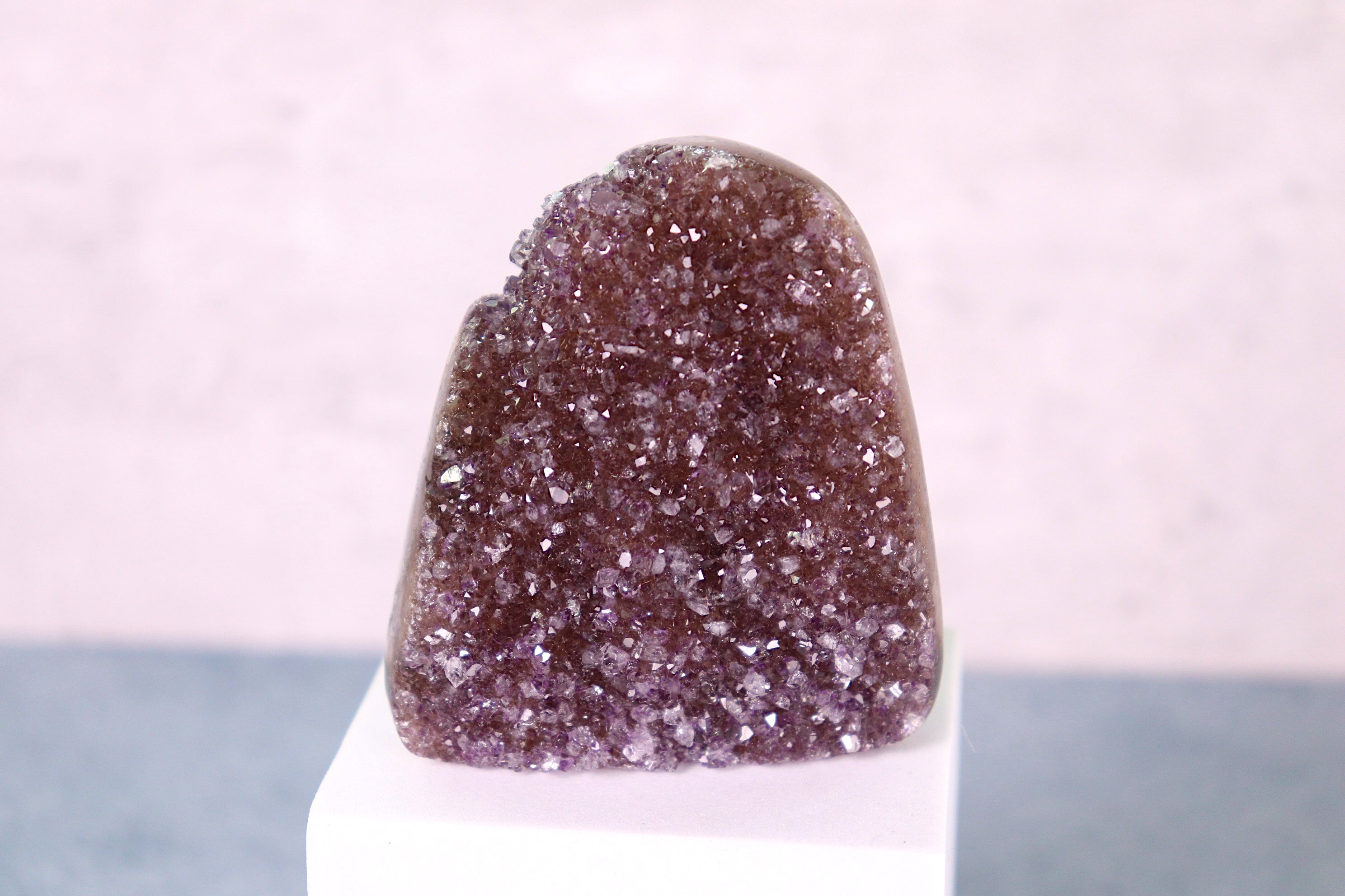 Amethyst  crystal on a white stand with a light pink background