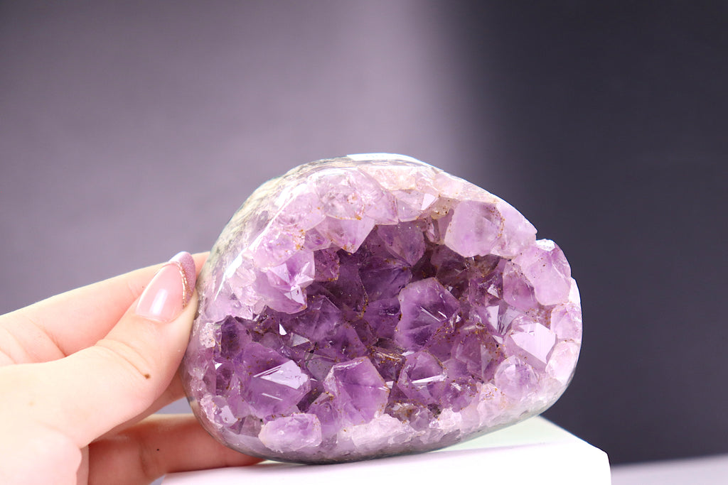 Amethyst crystal held by a hand against a dark background
