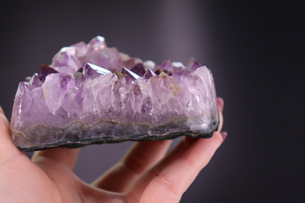 Hand holding a purple amethyst crystal with a dark background
