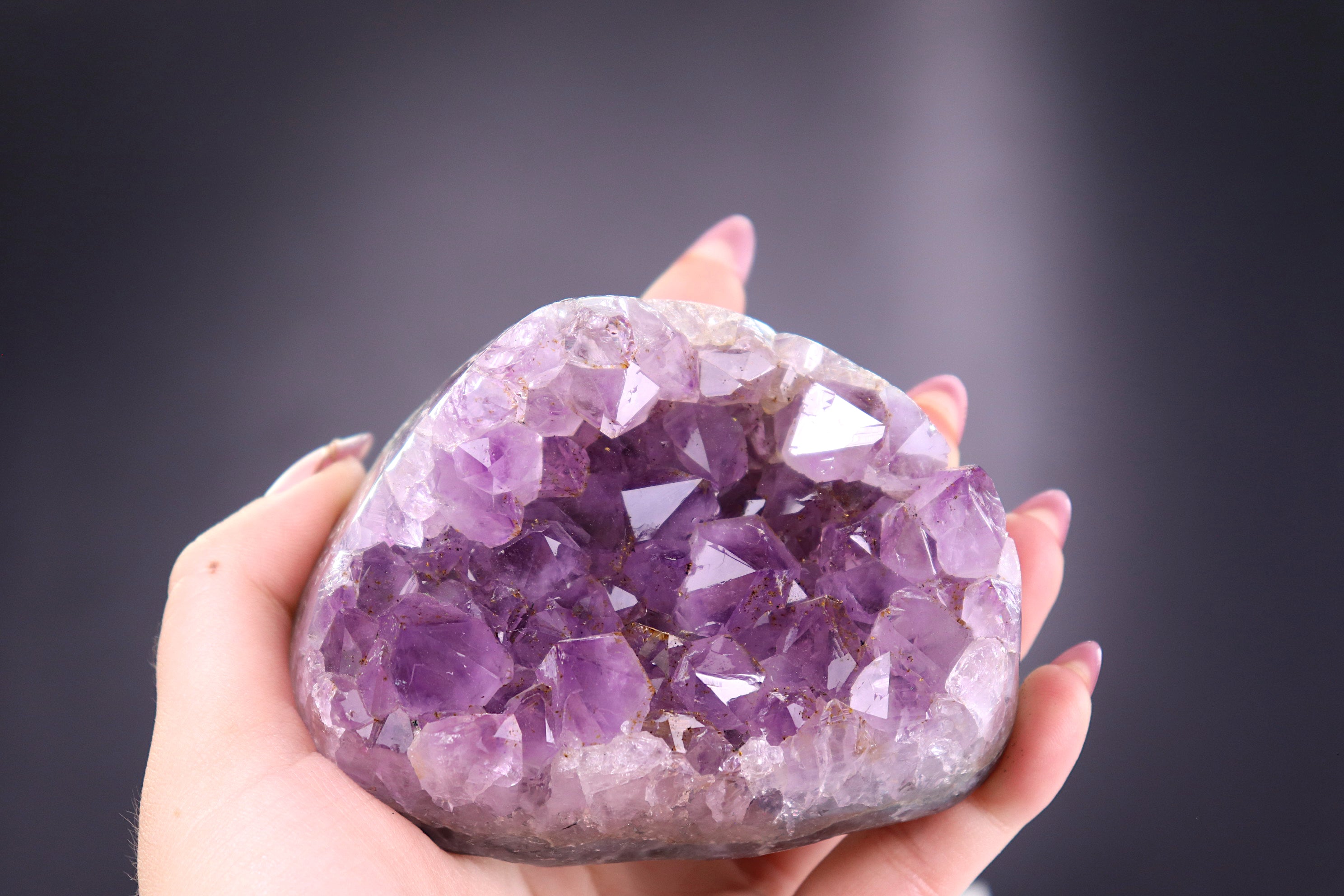 Hand holding a large amethyst crystal against a dark background
