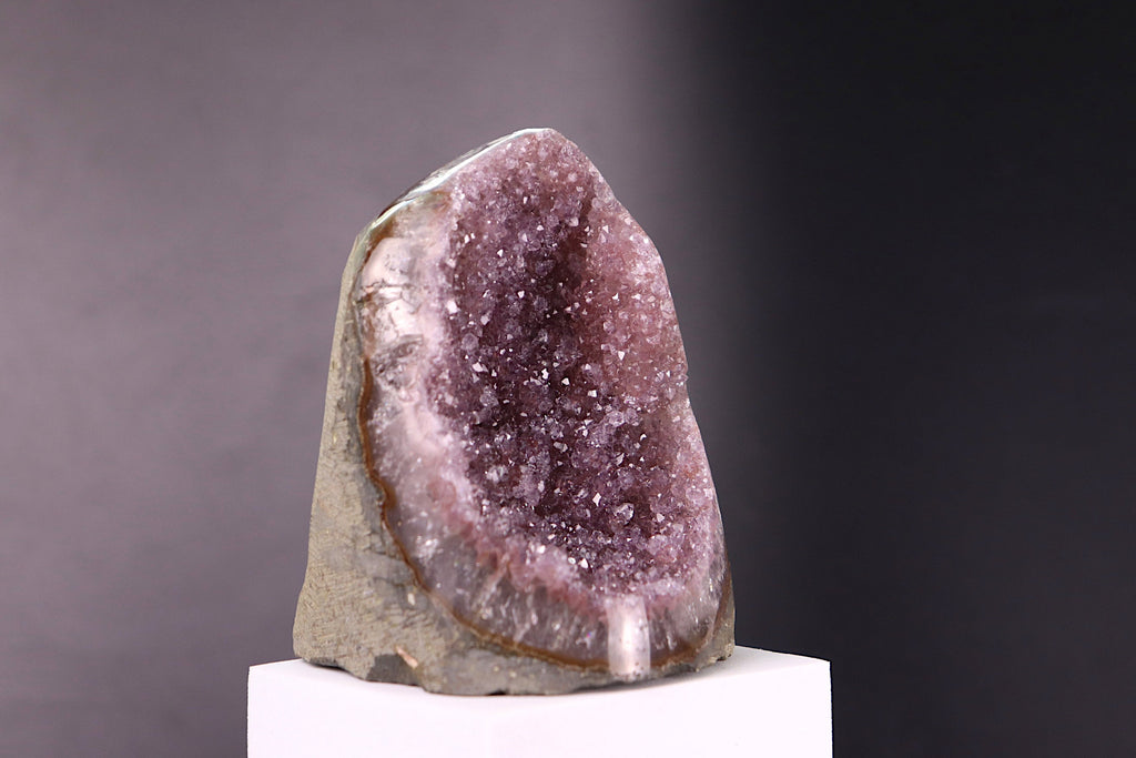 Amethyst geode on a white pedestal against a dark background