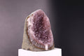 Amethyst geode on a white pedestal against a dark background