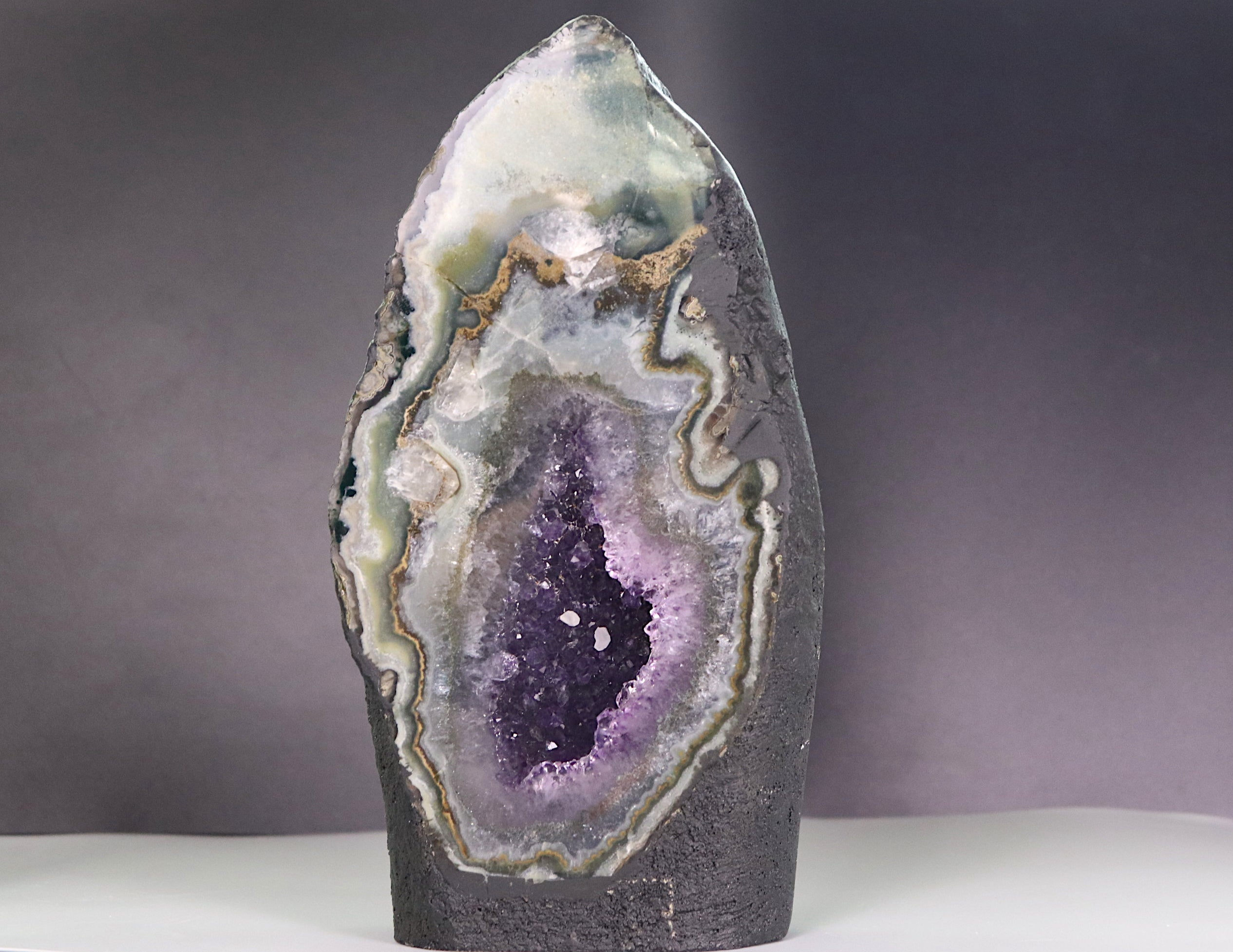 Geode with amethyst purple interior on surrounded by agate and calcite a gray background