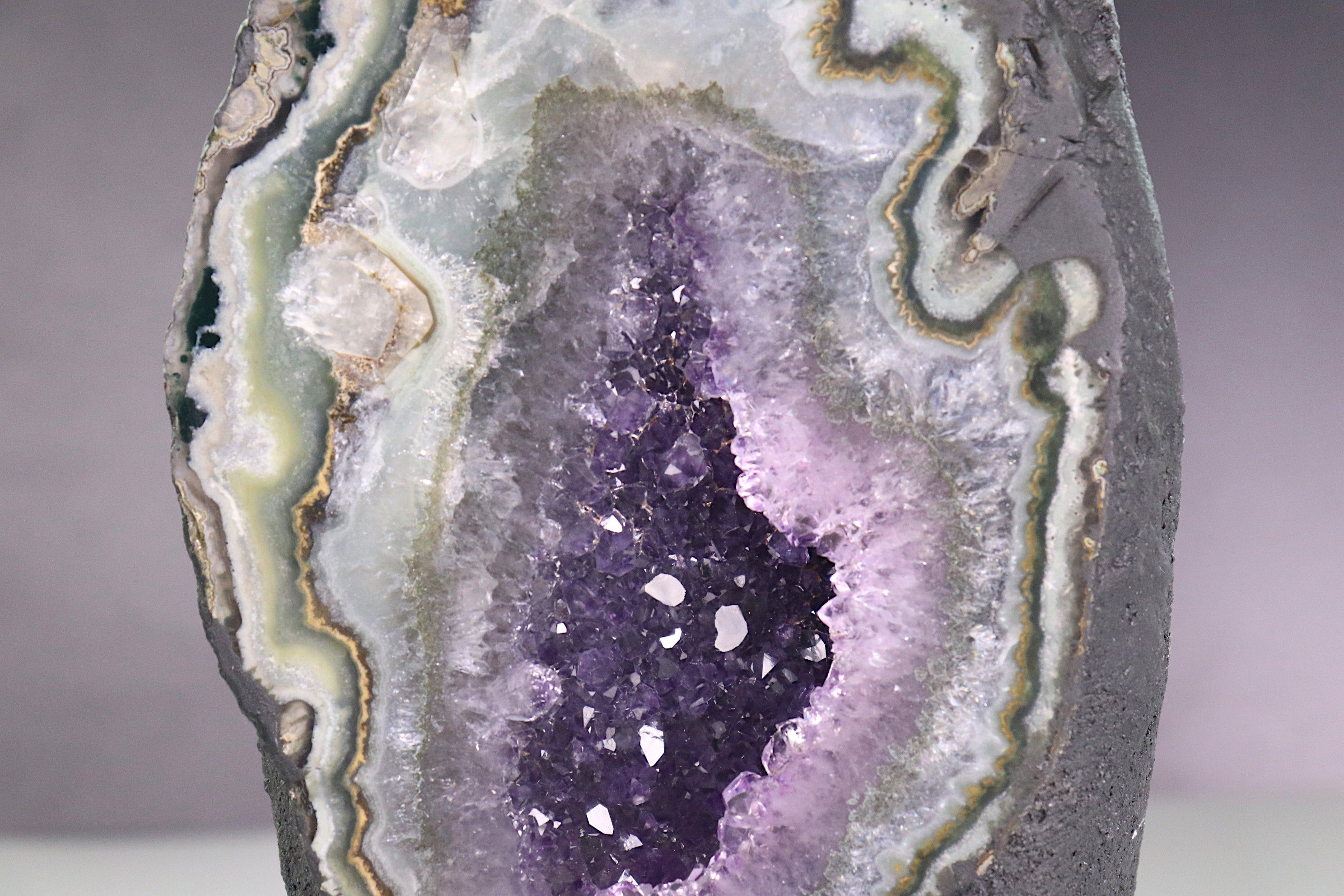 Close-up of a geode with purple amethyst surrounded by agate and calcite in front of a neutral background