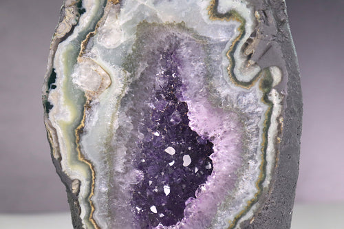 Close-up of a geode with purple amethyst surrounded by agate and calcite in front of a neutral background
