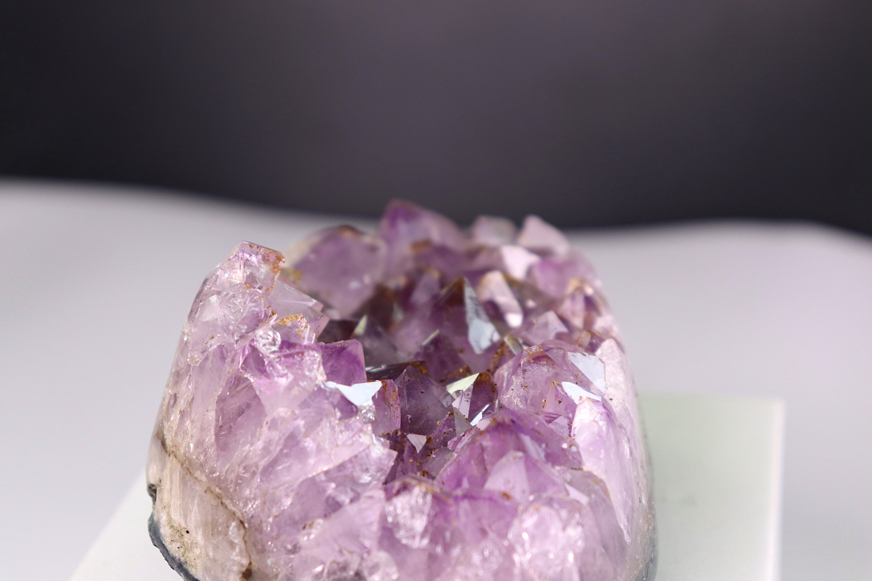Close-up of a amethyst crystal formation on a white surface with a dark background
