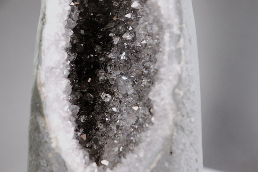 Close-up of a crystal formation with a dark core and amethyst crystals on a gray background