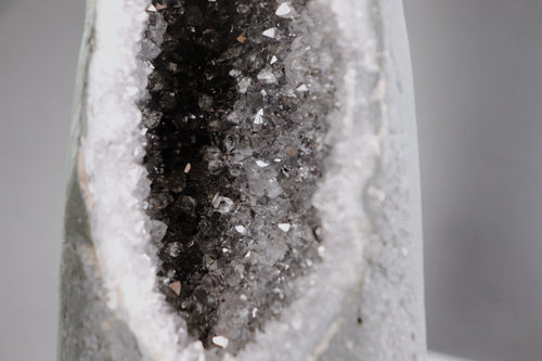 Close-up of a crystal formation with a dark core and amethyst crystals on a gray background