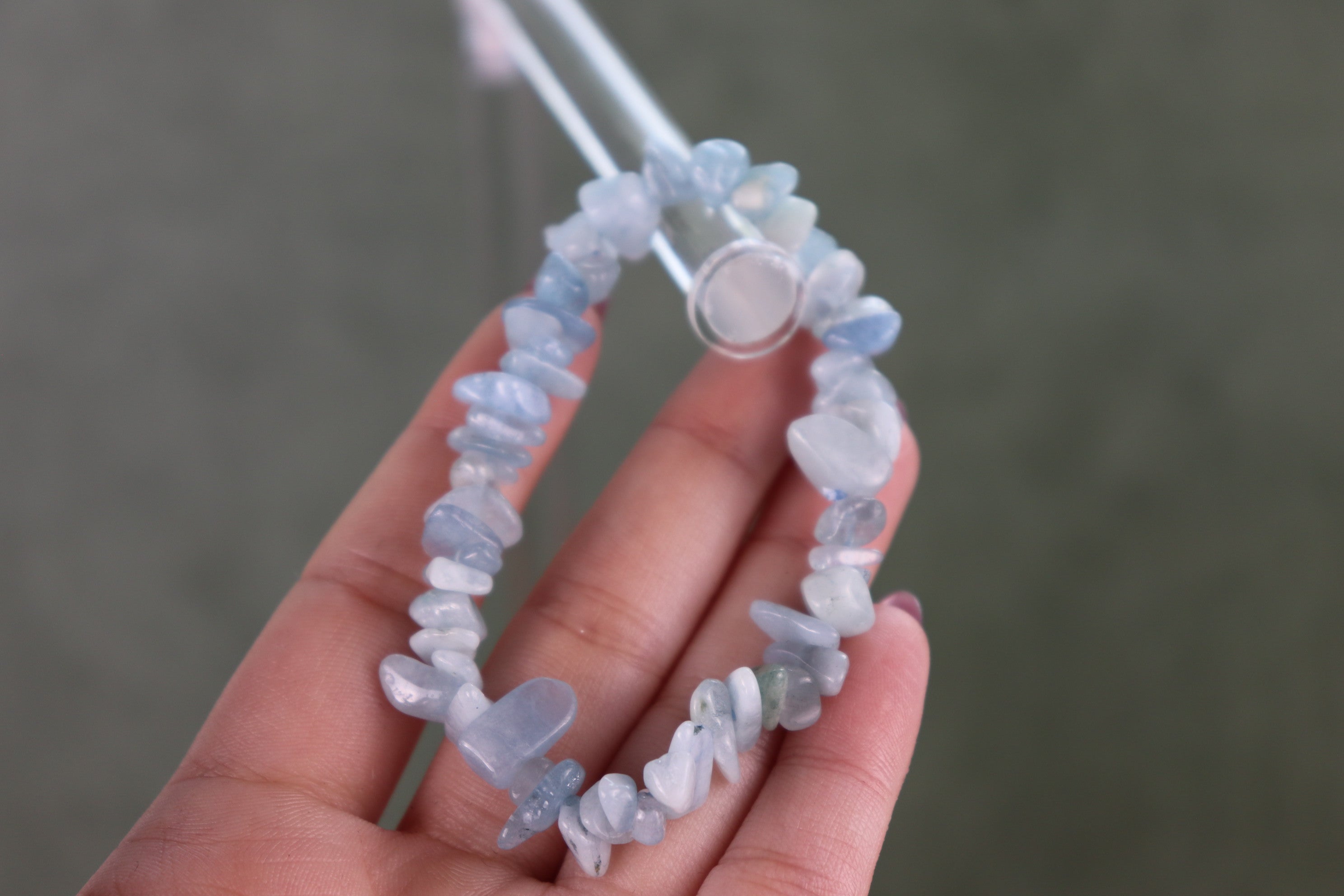 Hand holding a blue lace agate bracelet with blue and white beads against a gray background