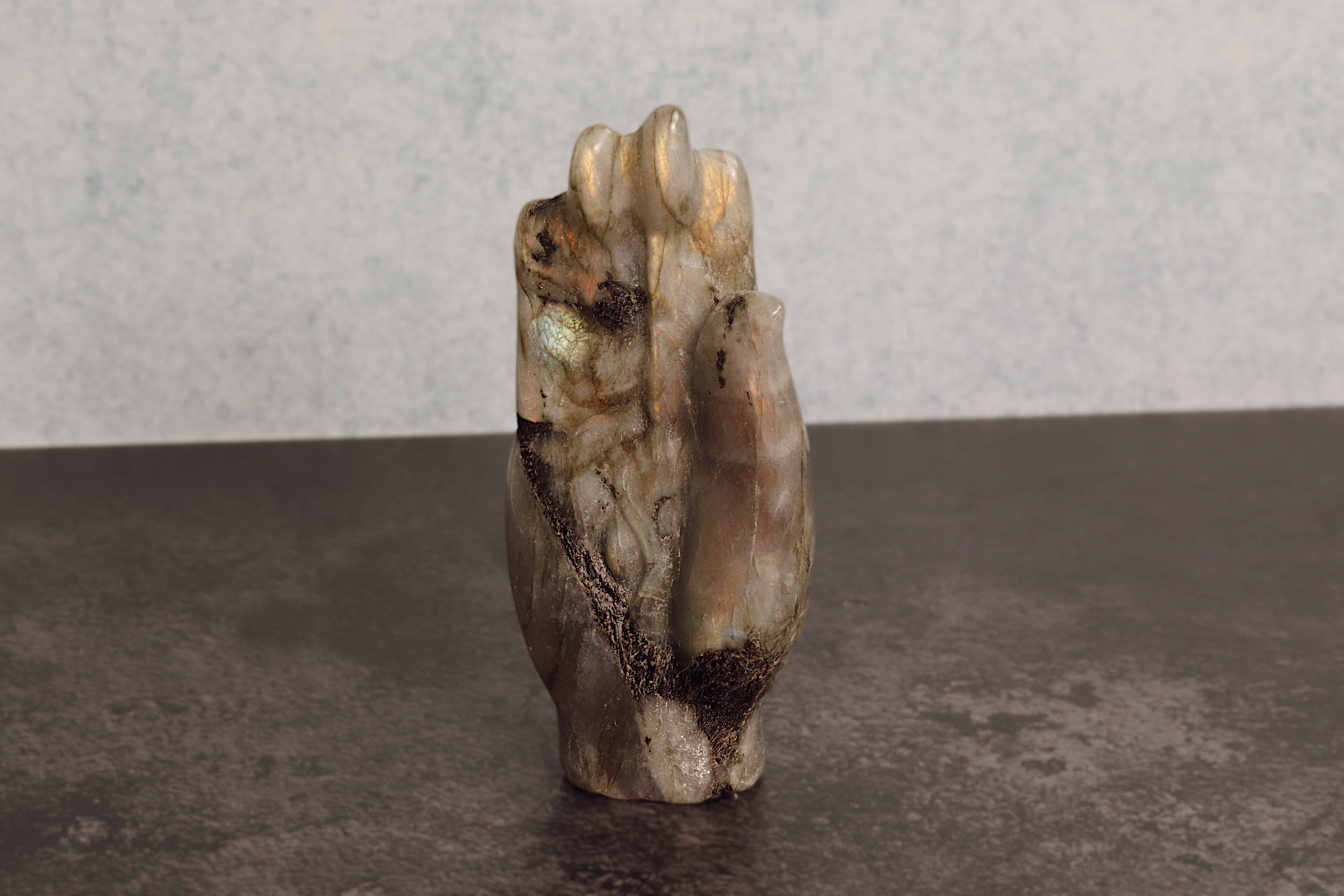 Carved labradorite stone figure of a hand on a dark surface with a gray background