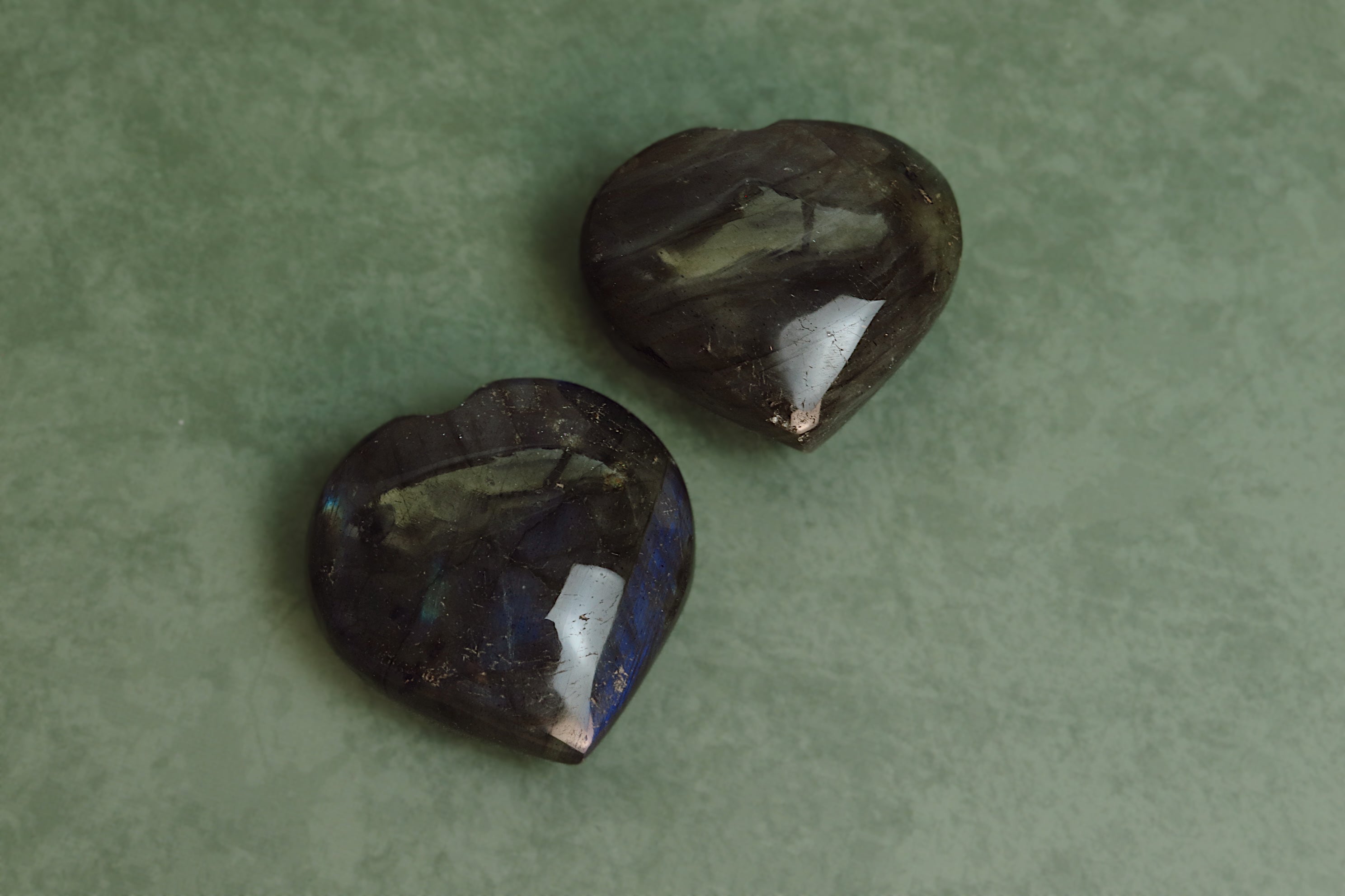 Two heart-shaped labradorite gemstones on a green background