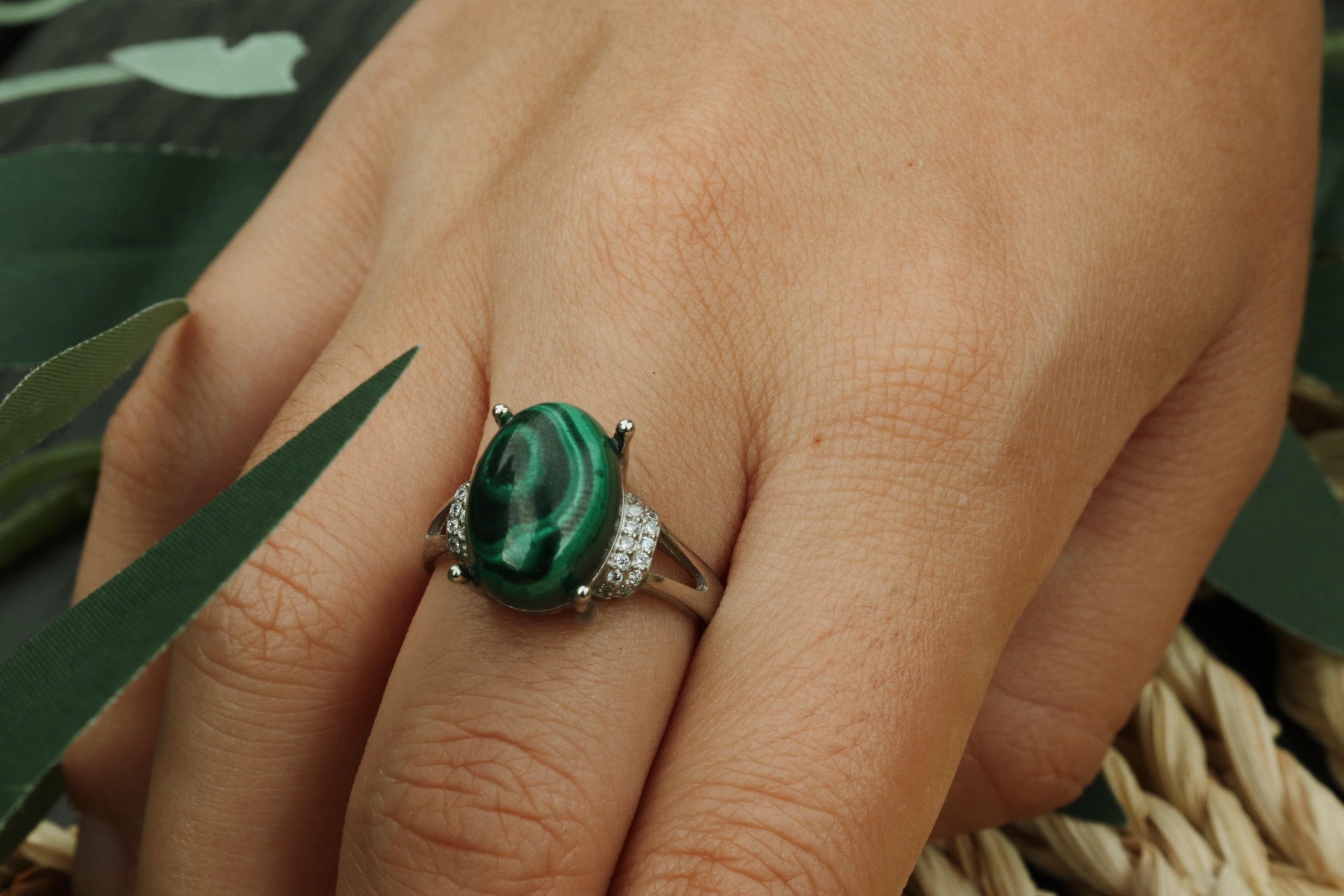 Close-up of a hand wearing a ring with a green malachite gemstone against a natural background
