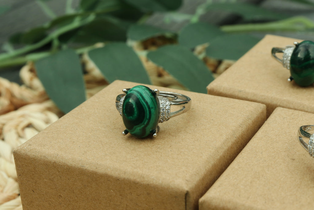 Malachite Green gemstone ring on a brown jewelry box with green leaves in the background