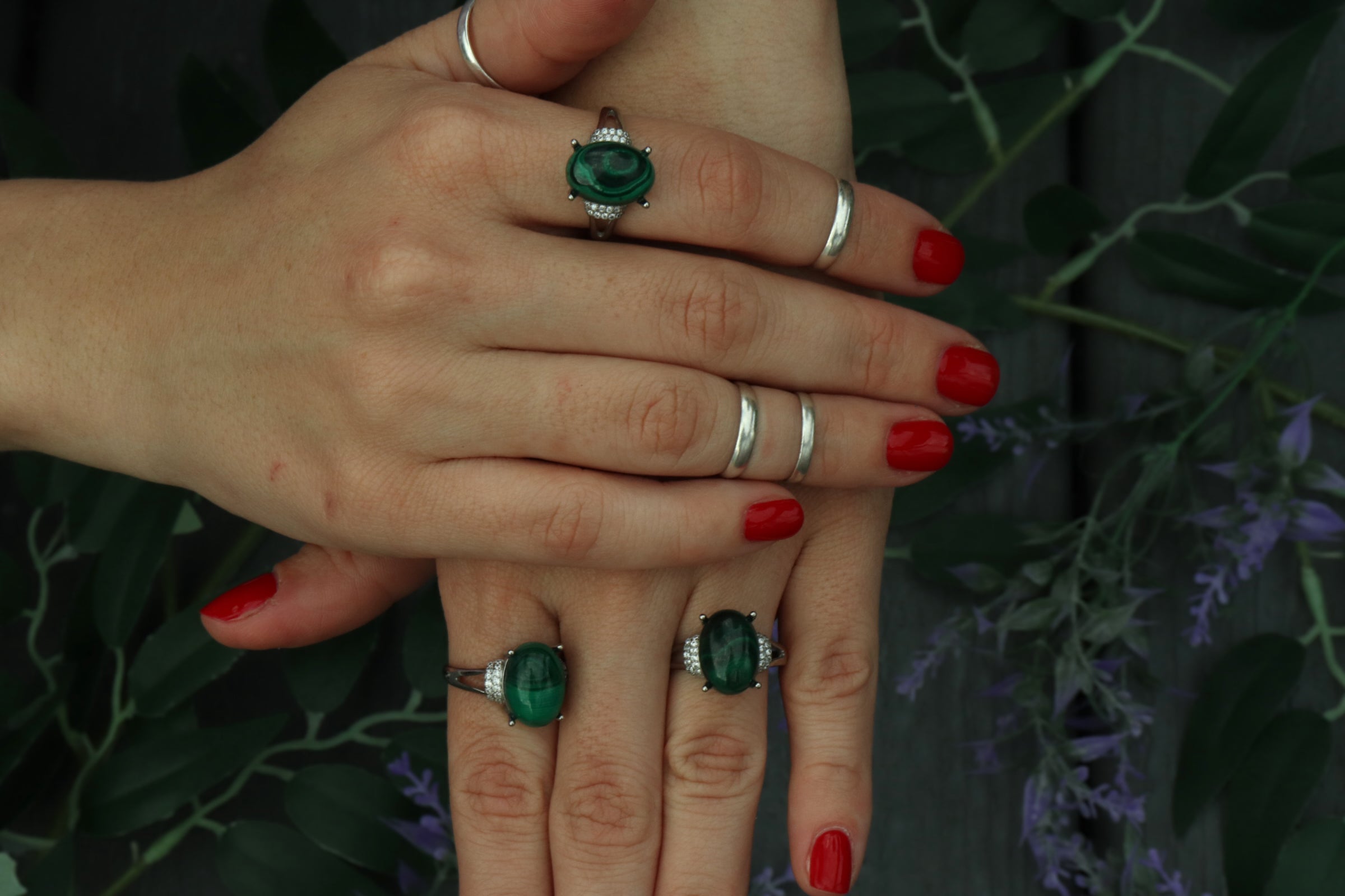 Close-up of hands with malachite green rings on fingers against a dark background