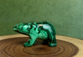 Green malachite bear figurine on a wooden surface with a green background