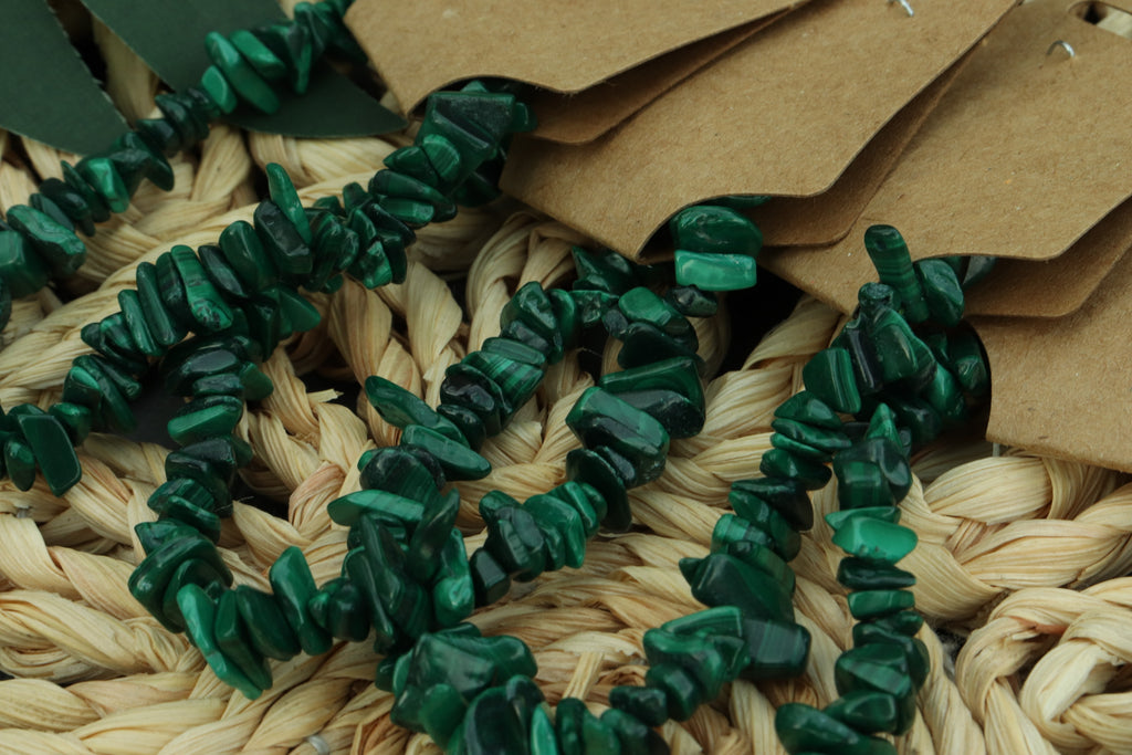 Green malachite chip bracelet on a woven surface with brown paper tags.