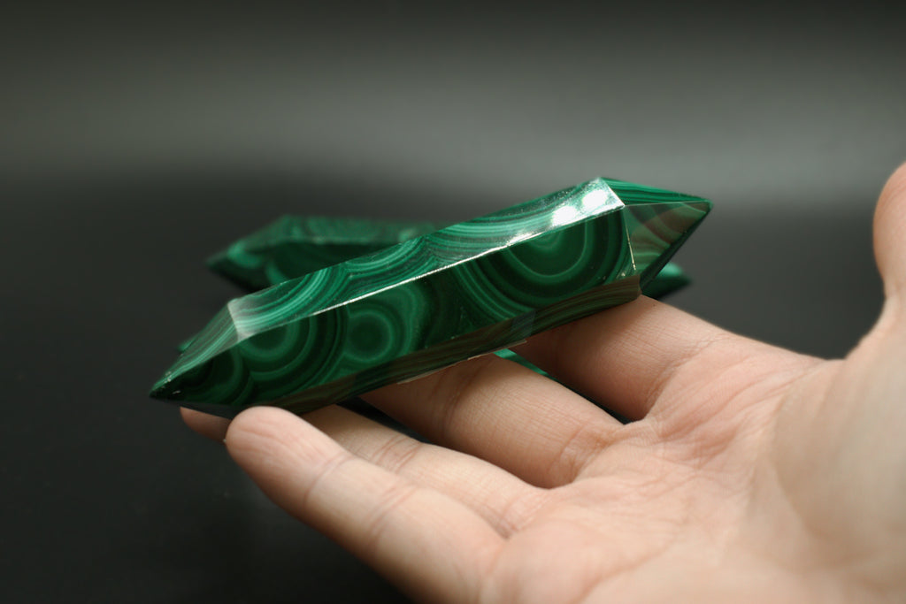 Green malachite crystal double terminated held in a hand against a dark background