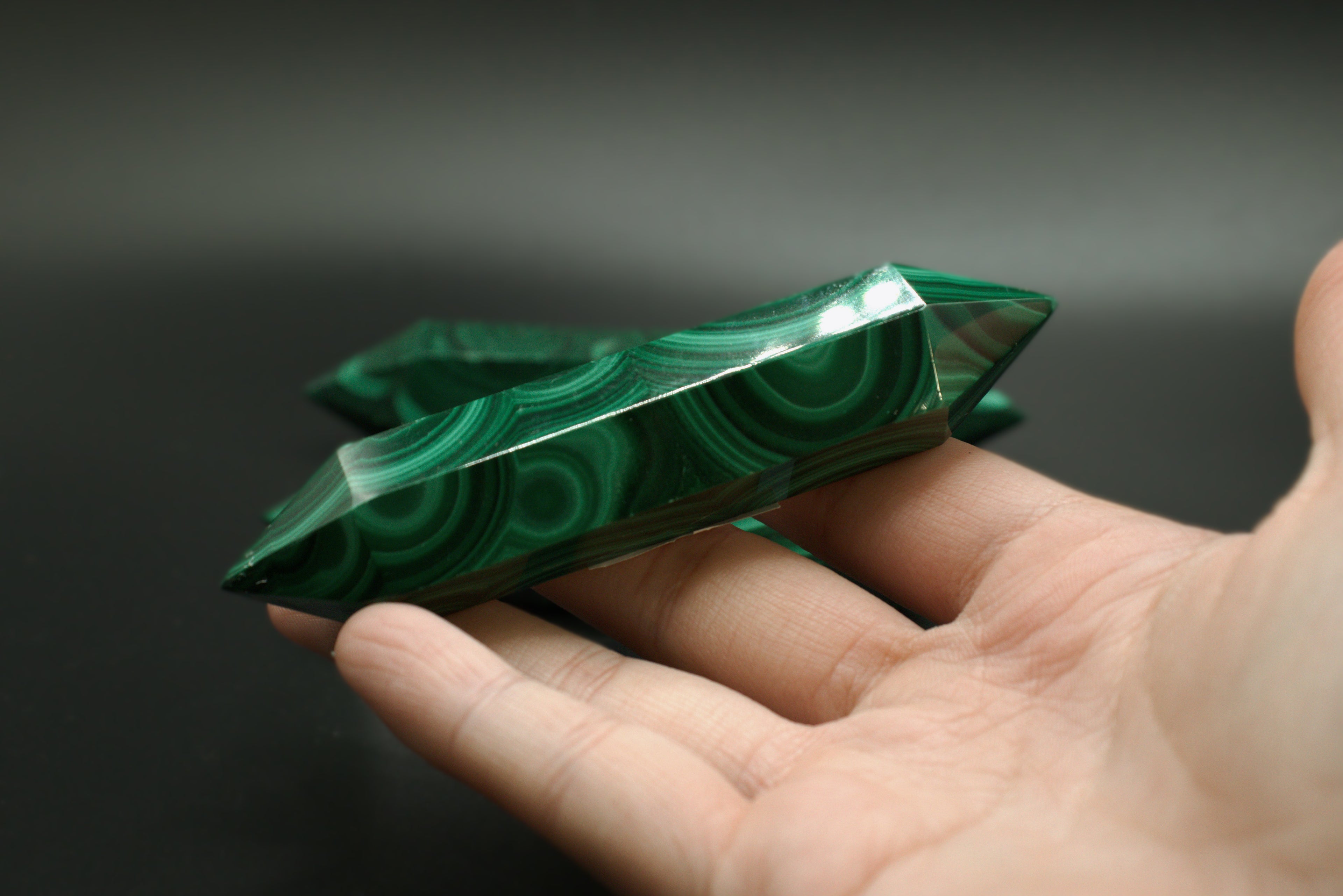 Green malachite crystal double terminated held in a hand against a dark background