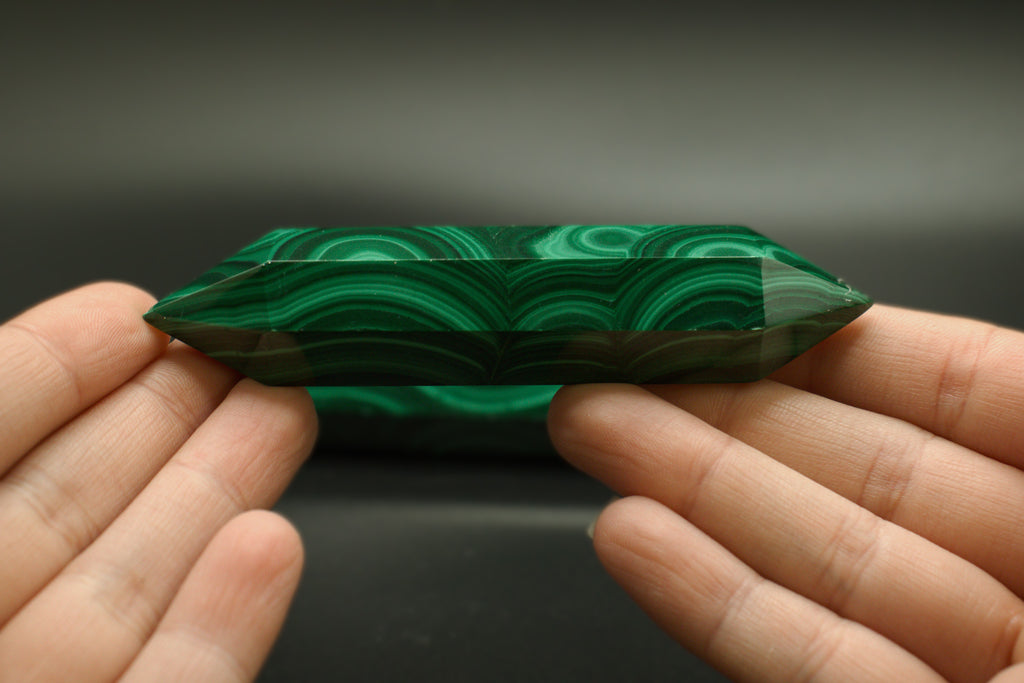 Green malachite crystal held between two hands against a dark background